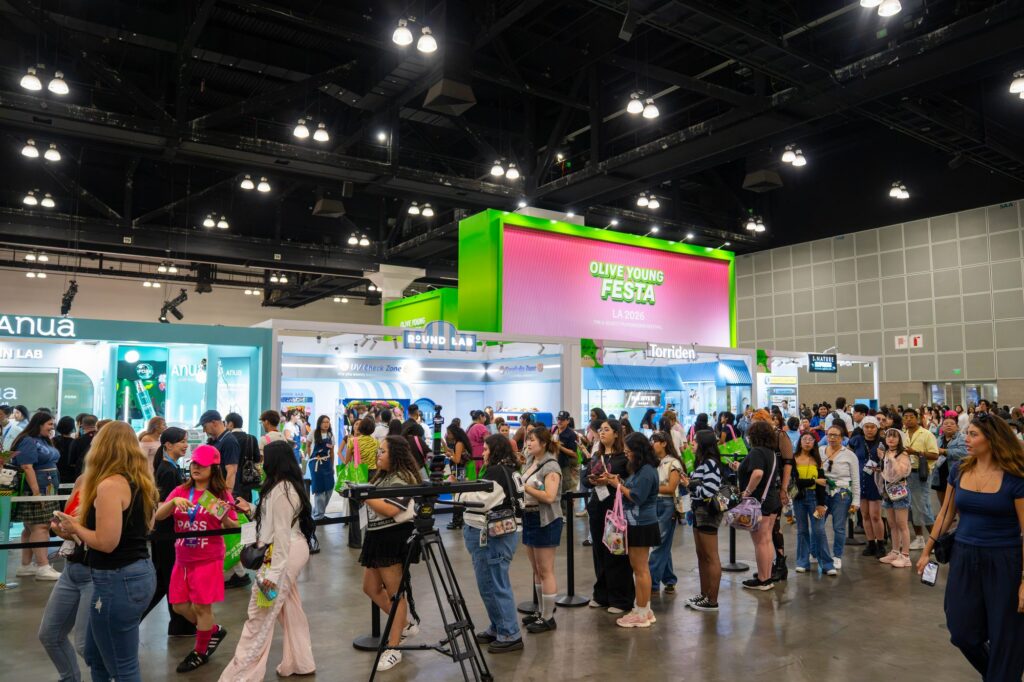 Wide view of Anua, Round Lab and Torriden booths beneath the Olive Young Festa tower sign at KCON LA 2026